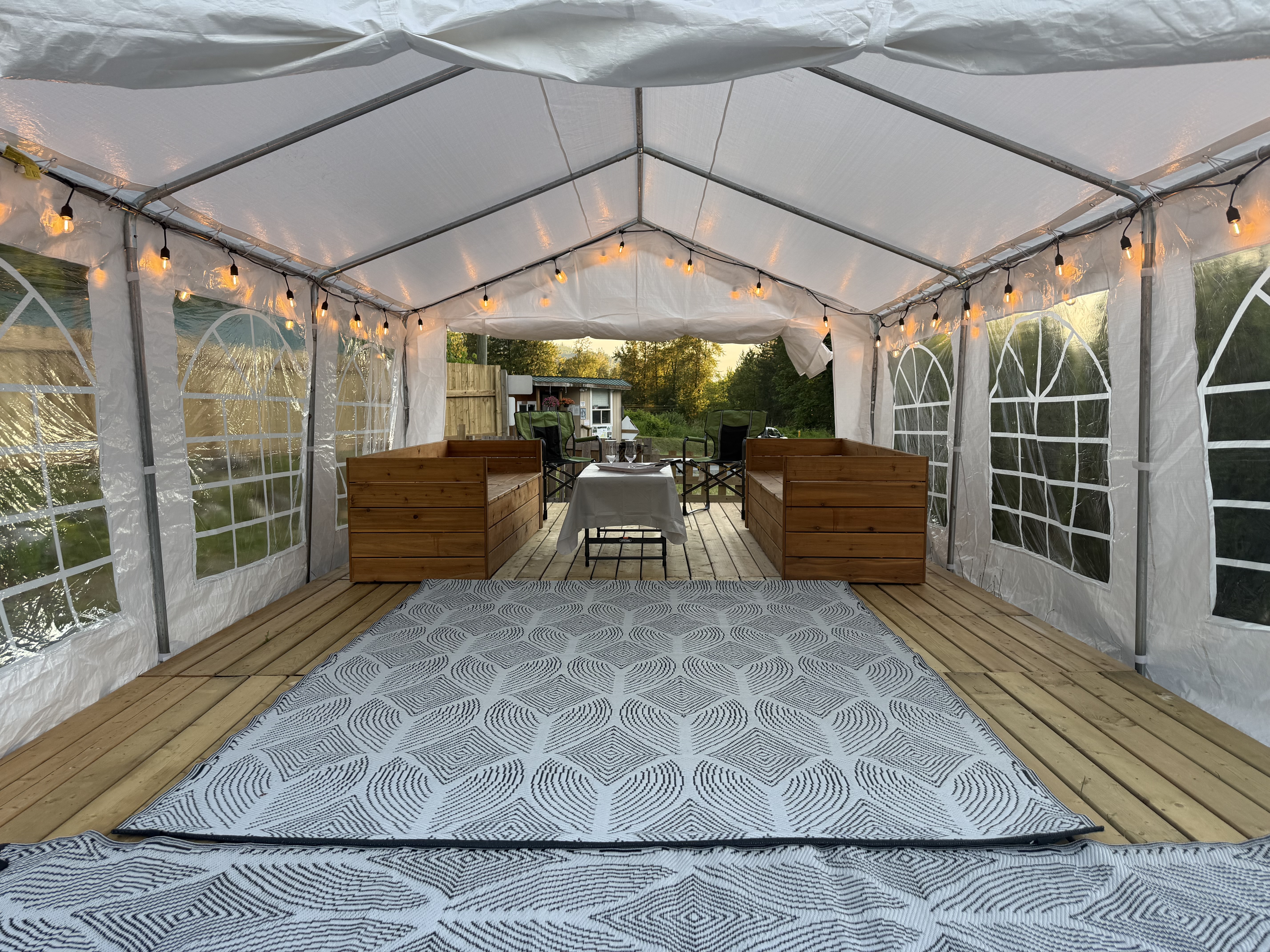 Inside the Pavilion: a covered, string-lit tent on a wood deck with bench seating and an outdoor rug